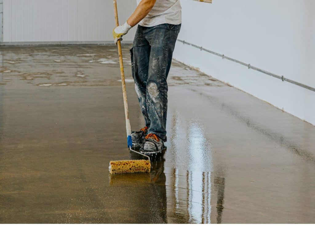 person is coating the floor, dressed in a white t-shirt and jeans, wearing gloves but upper body is not seen