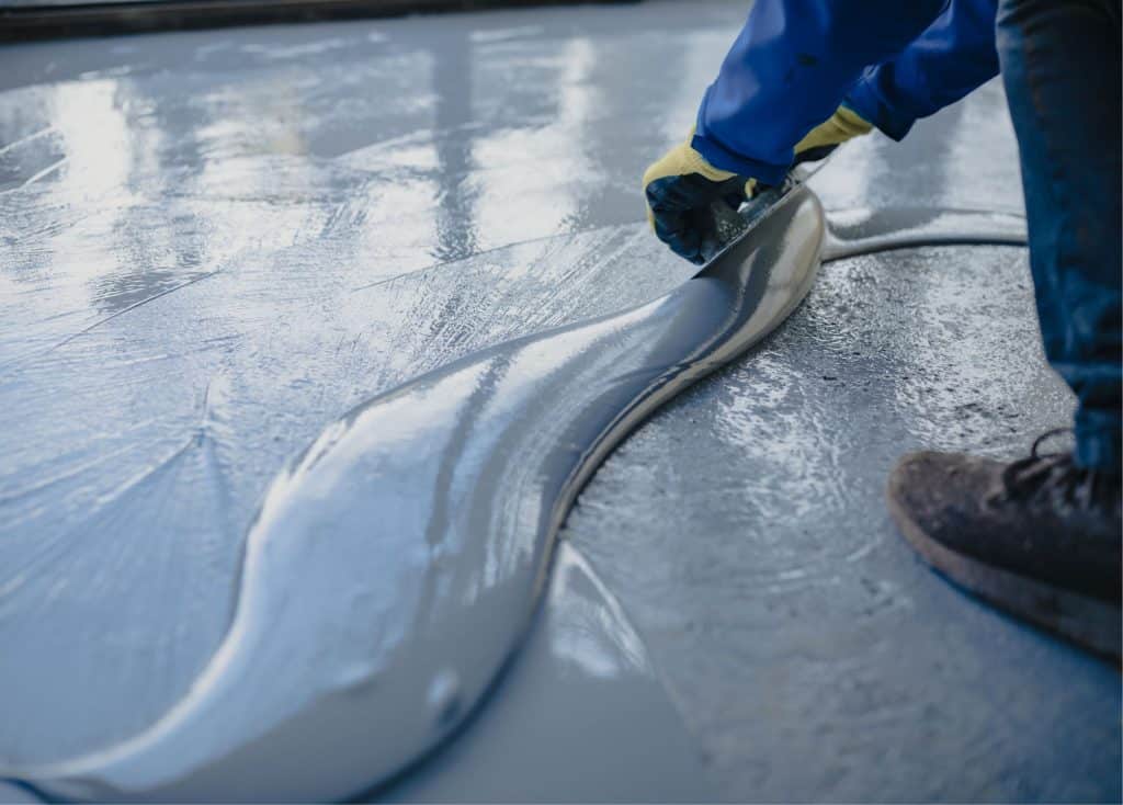 floor is being coated with gray coating, there is a hand at work and a shoe